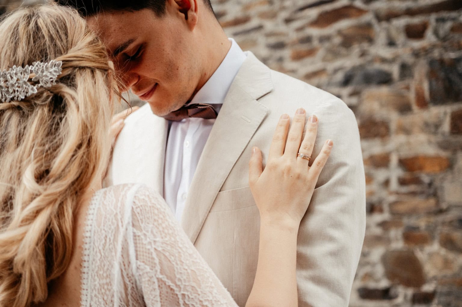 Hochzeitspaar umarmt sich liebevoll vor einer Steinmauer, intime Stimmung.