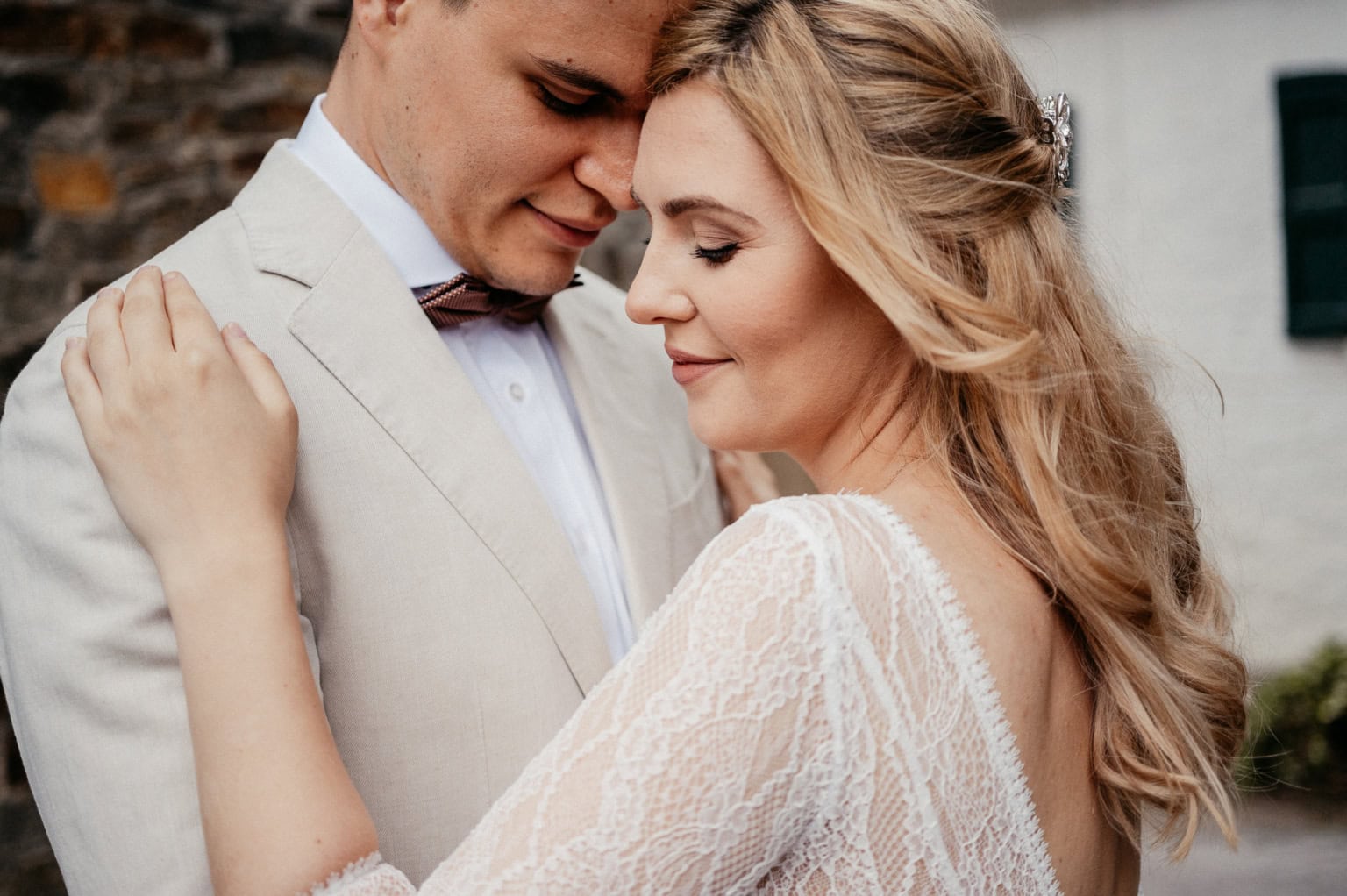 Hochzeitspaar umarmt sich liebevoll vor einem Haus, strahlt Glück und Liebe aus.