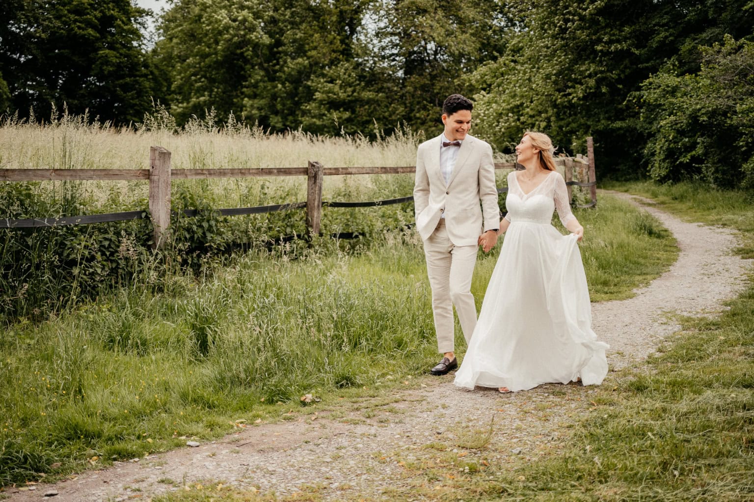 Hochzeitspaar beim Spaziergang im Grünen, Hand in Hand auf einem Weg im Park.