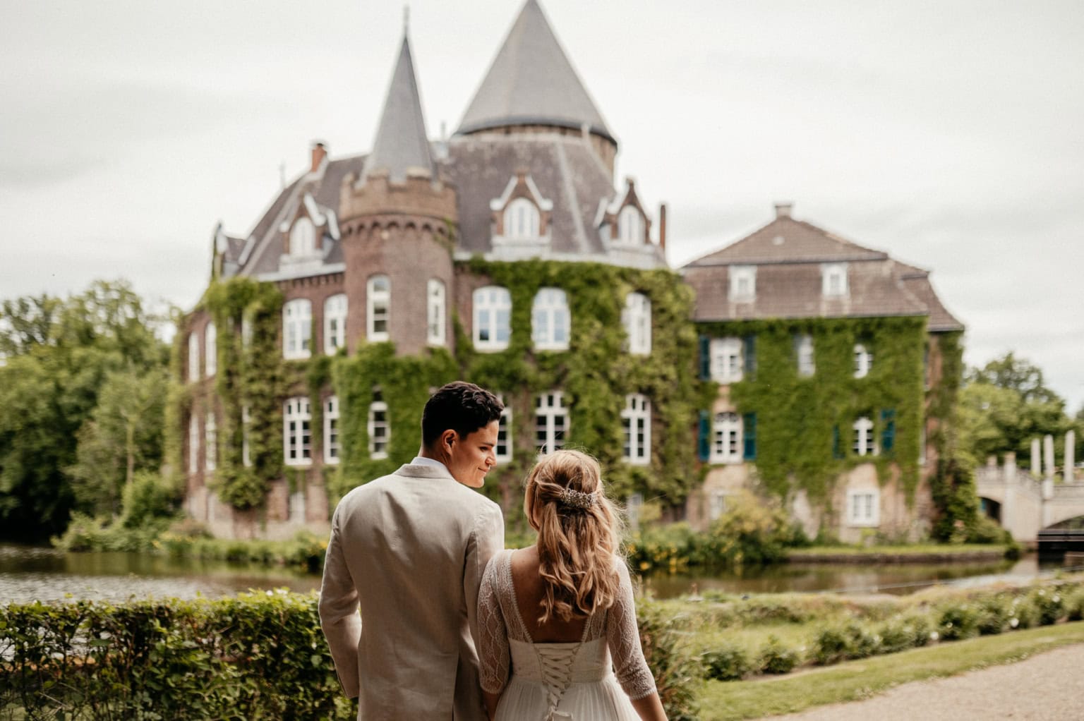 Schloss im Park mit Brautpaar im Vordergrund, romantischer Moment bei Hochzeit im Grünen.