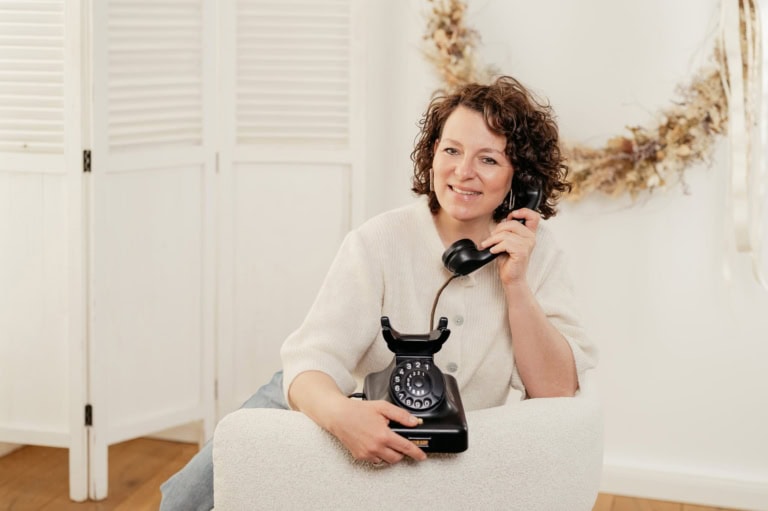 Frau spricht am Festnetztelefon im Wohnzimmer.