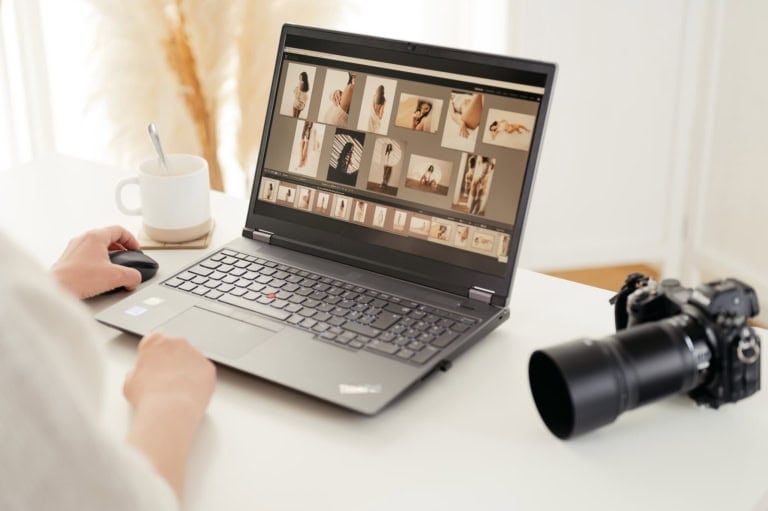 Person bearbeitet Fotos am Laptop, Kamera liegt daneben.