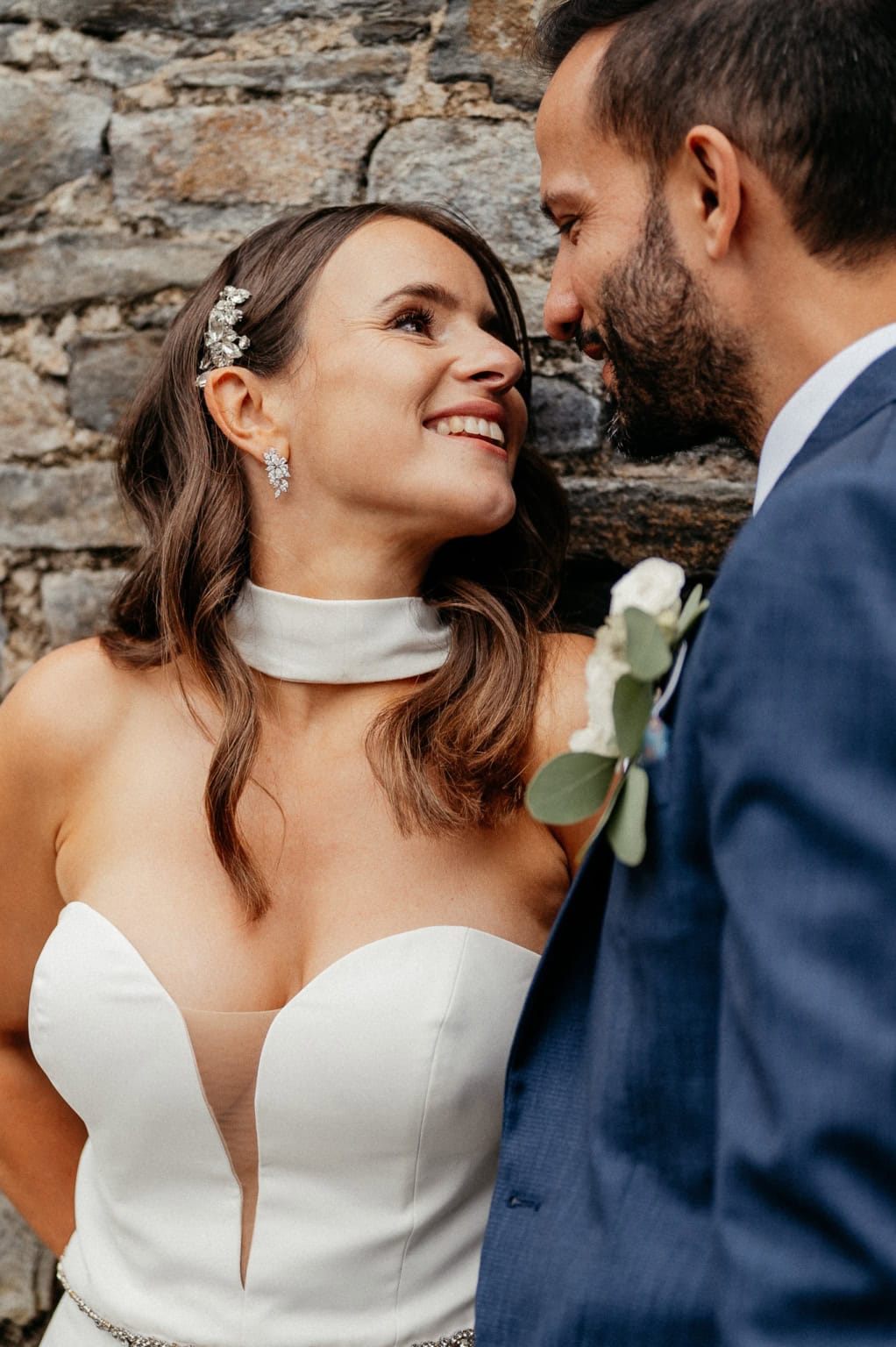 Hochzeitspaar schaut sich verliebt an vor einer alten Steinmauer, strahlende Gesichter, romantischer.