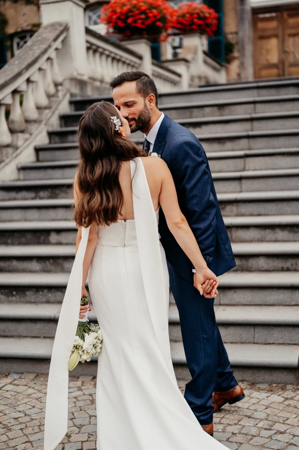 Hochzeitspaar auf Treppe vor historischem Gebäude, Händchen haltend, verliebt.