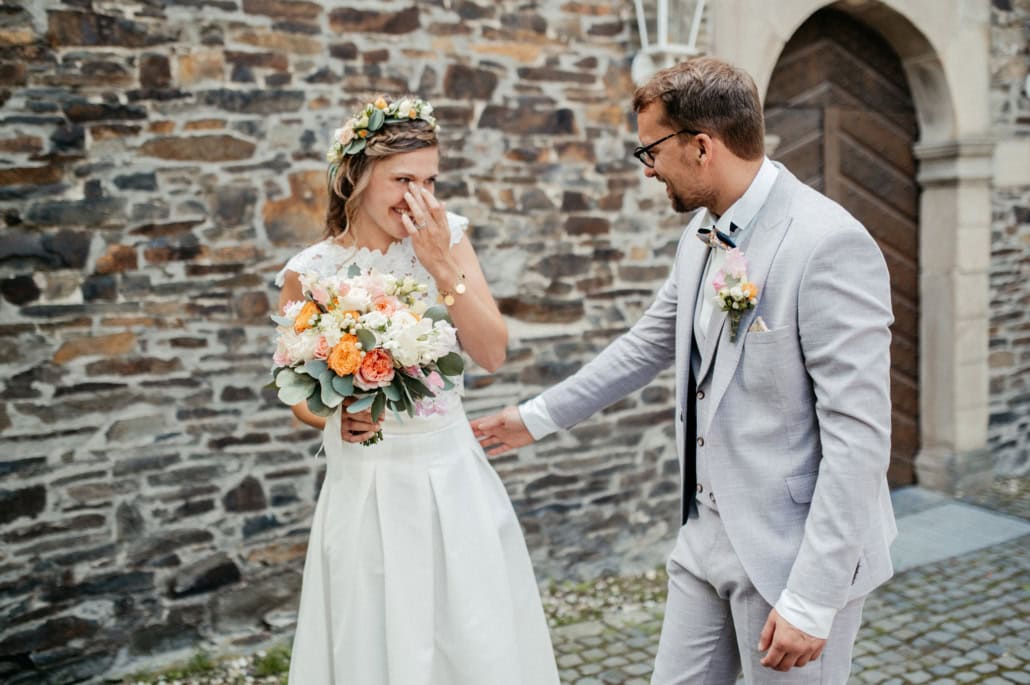 Hochzeit im Freien: Braut und Bräutigam vor einer Steinmauer, emotionaler Moment.