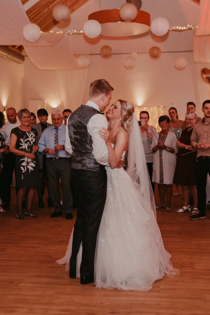 Romantischer Moment des Hochzeitstanzes mit Gästen im Hintergrund.