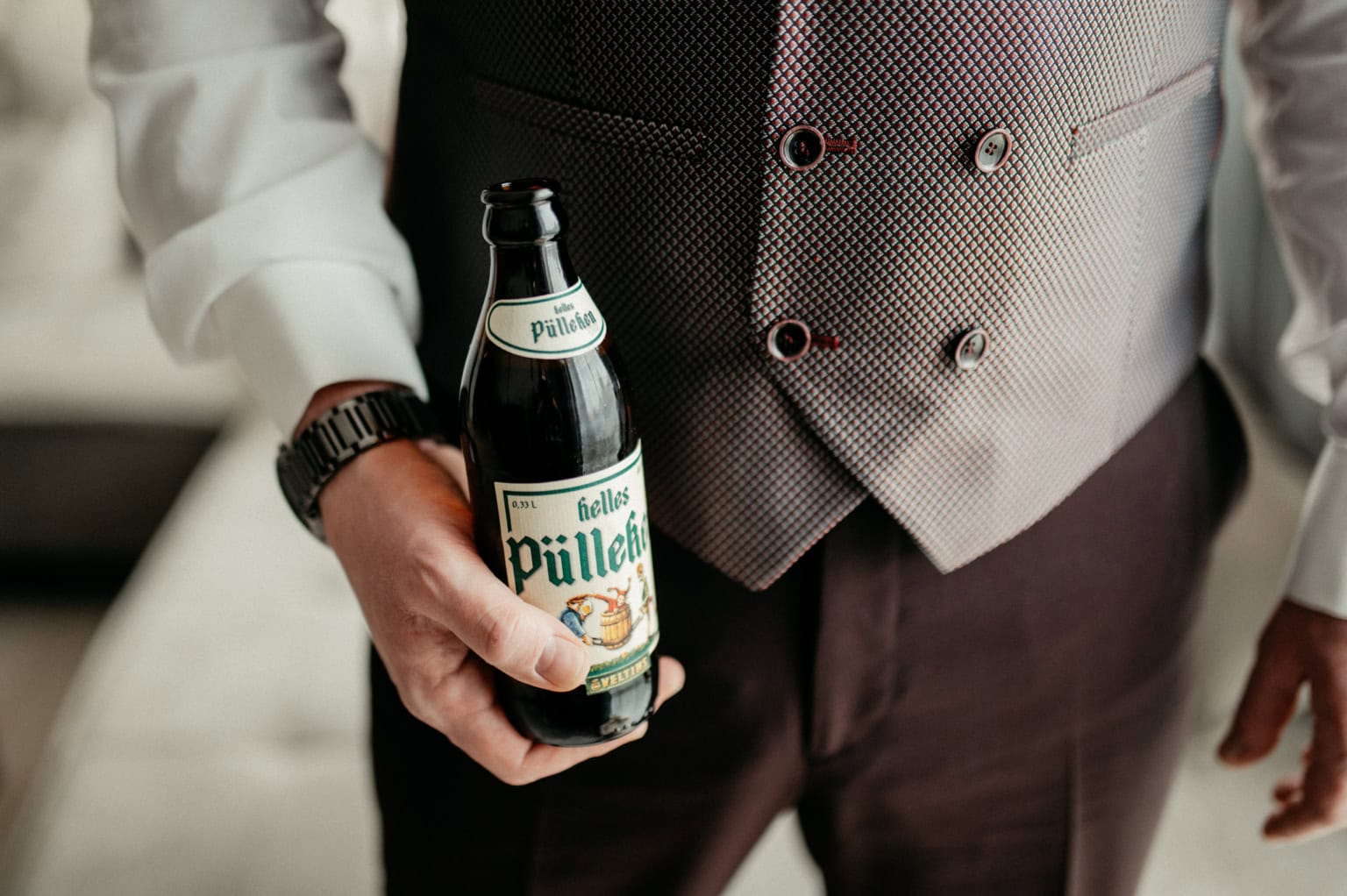 Mann in Anzug hält Bierflasche in der Hand.
