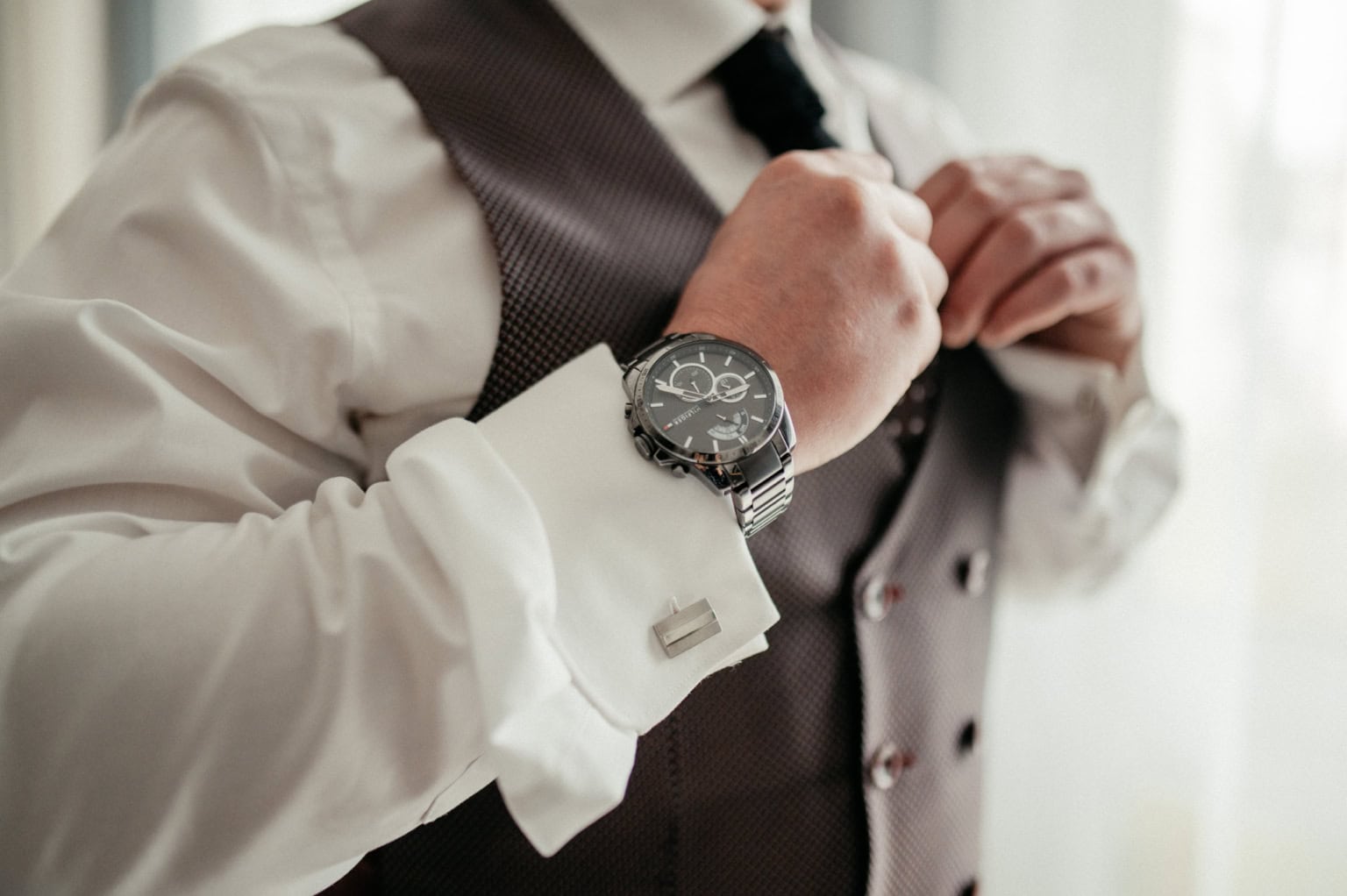 Herren in formellem Anzug passt seine Krawatte an, elegante Uhr sichtbar am Handgelenk.