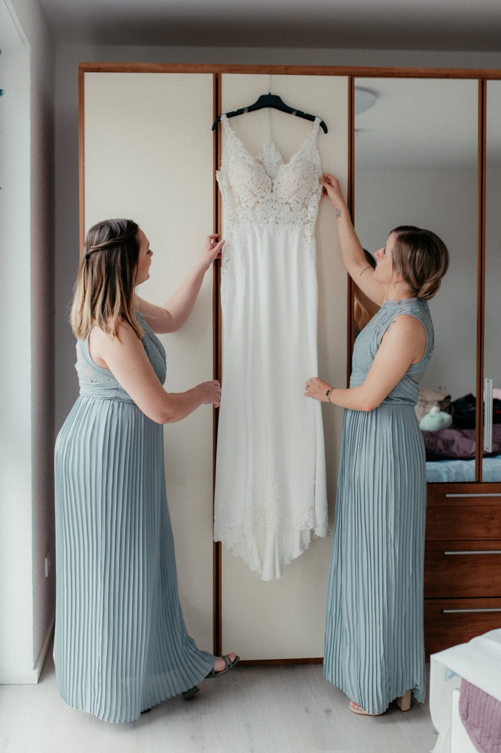 Zwei Frauen bewundern ein elegantes Hochzeitskleid im Schlafzimmer.