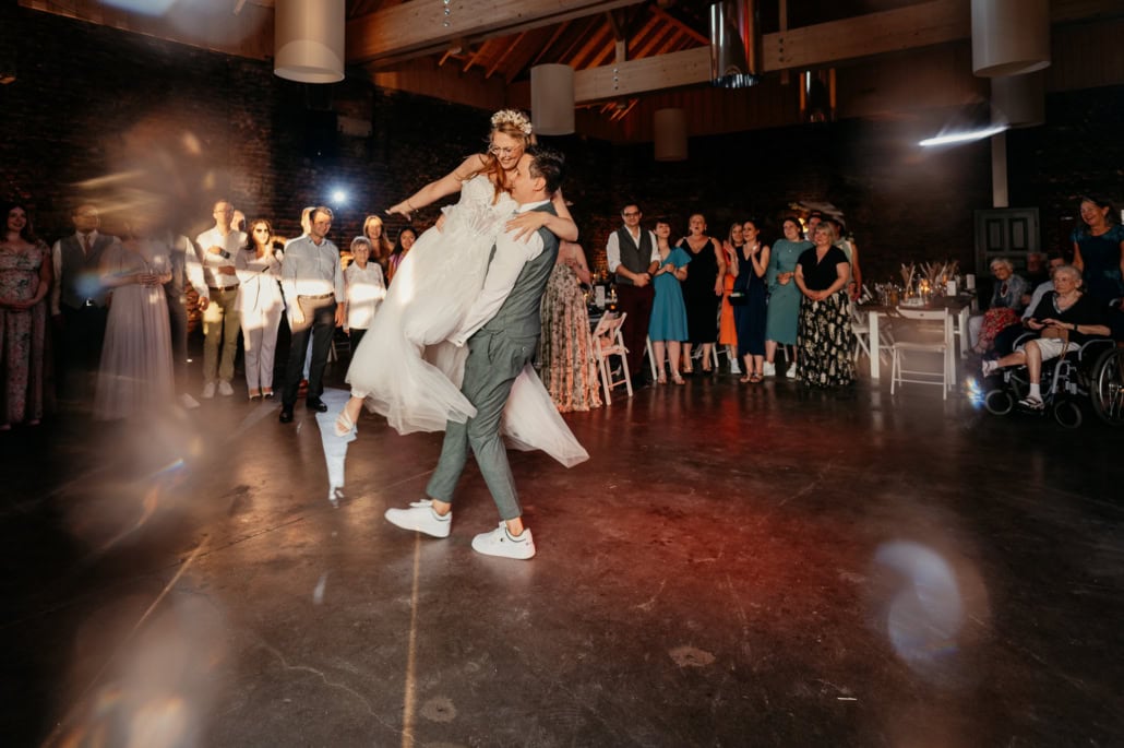 Hochzeitspaar tanzt im festlichen Rahmen mit Gästen im Hintergrund.