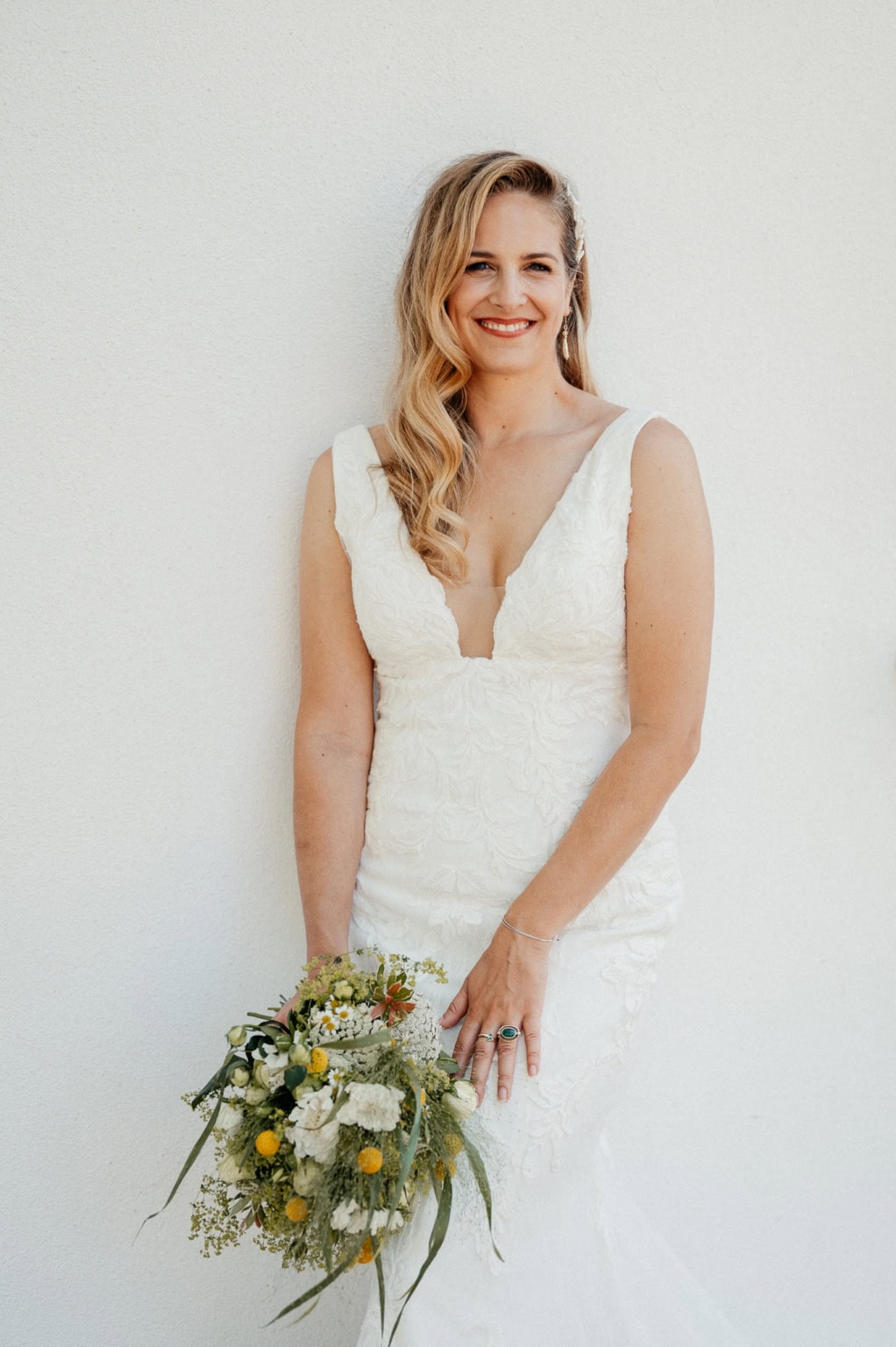 Braut in weißem Hochzeitskleid hält Blumenstrauß und lächelt.