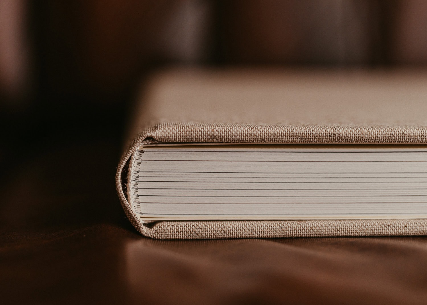 Buch mit beige Einband und sichtbaren Seiten, auf dunklem Tisch.