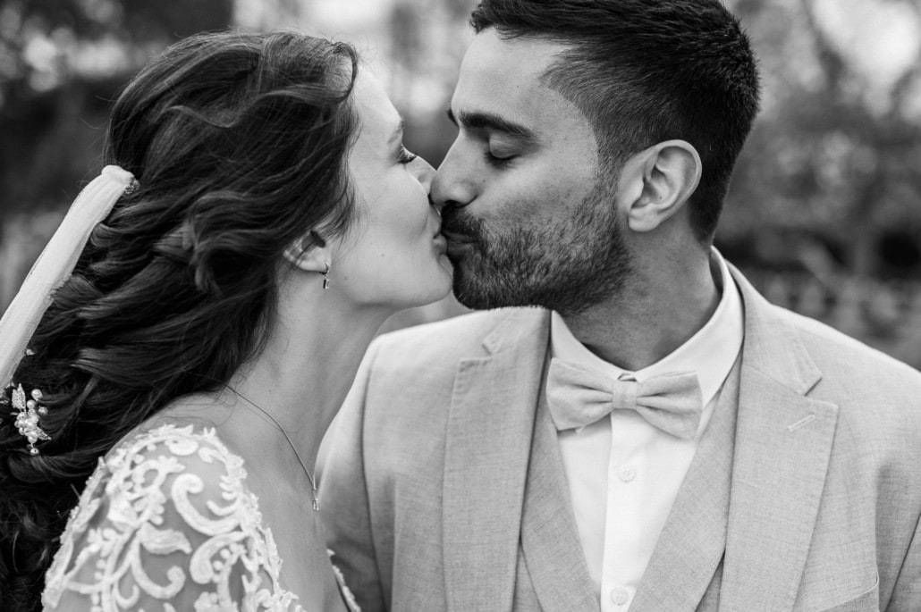 Hochzeitspaar küsst sich liebevoll im Freien, romantischer Moment bei einer Hochzeit.