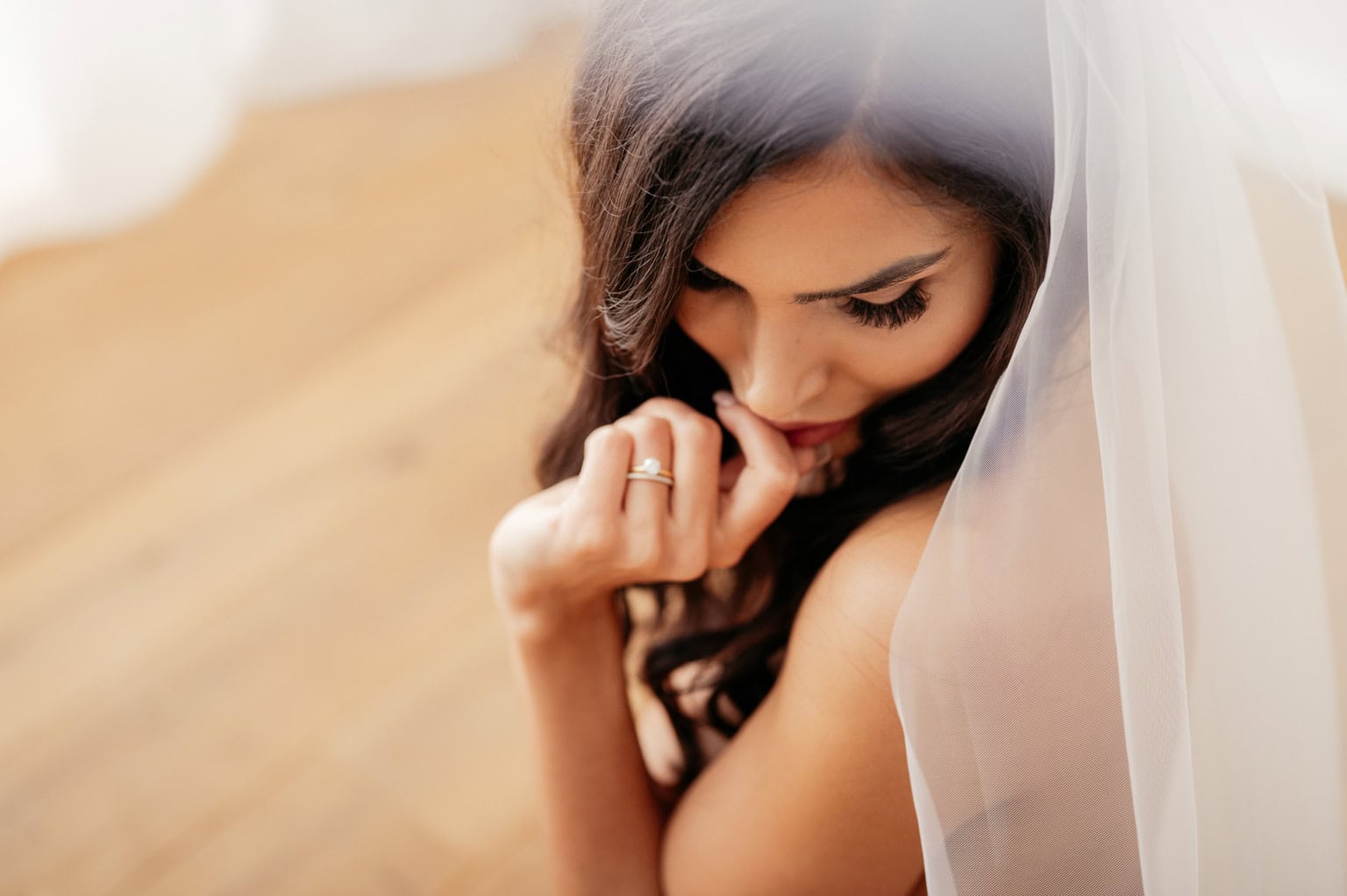 Hochzeitsporträt einer jungen Braut mit Schleier, die nachdenklich den Kopf senkt.