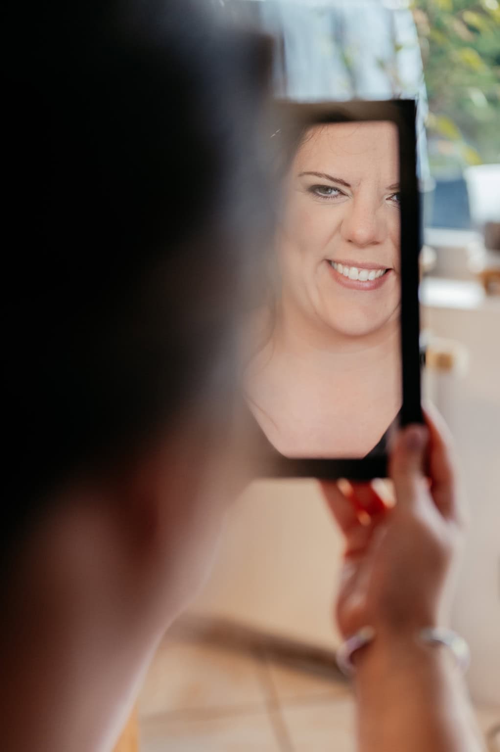 Frau, die sich im Spiegel betrachtet und lächelt, während sie ein Selfie macht.