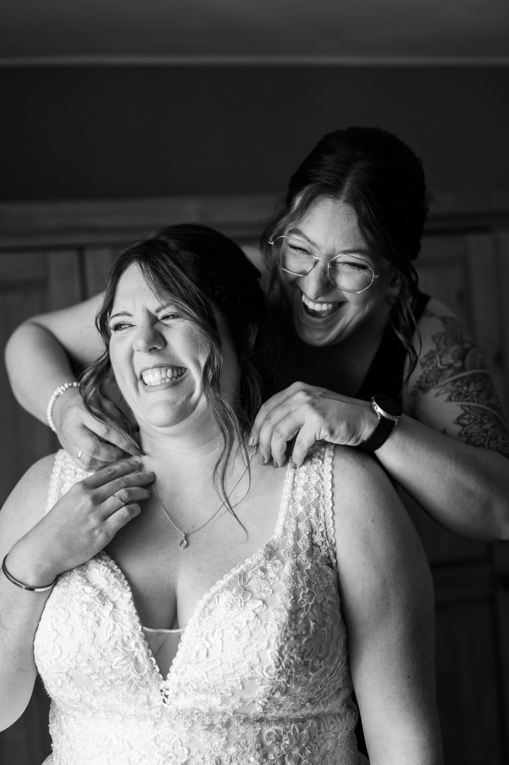 Zwei Frauen bei einer Hochzeit, eine umarmt die andere lachend.