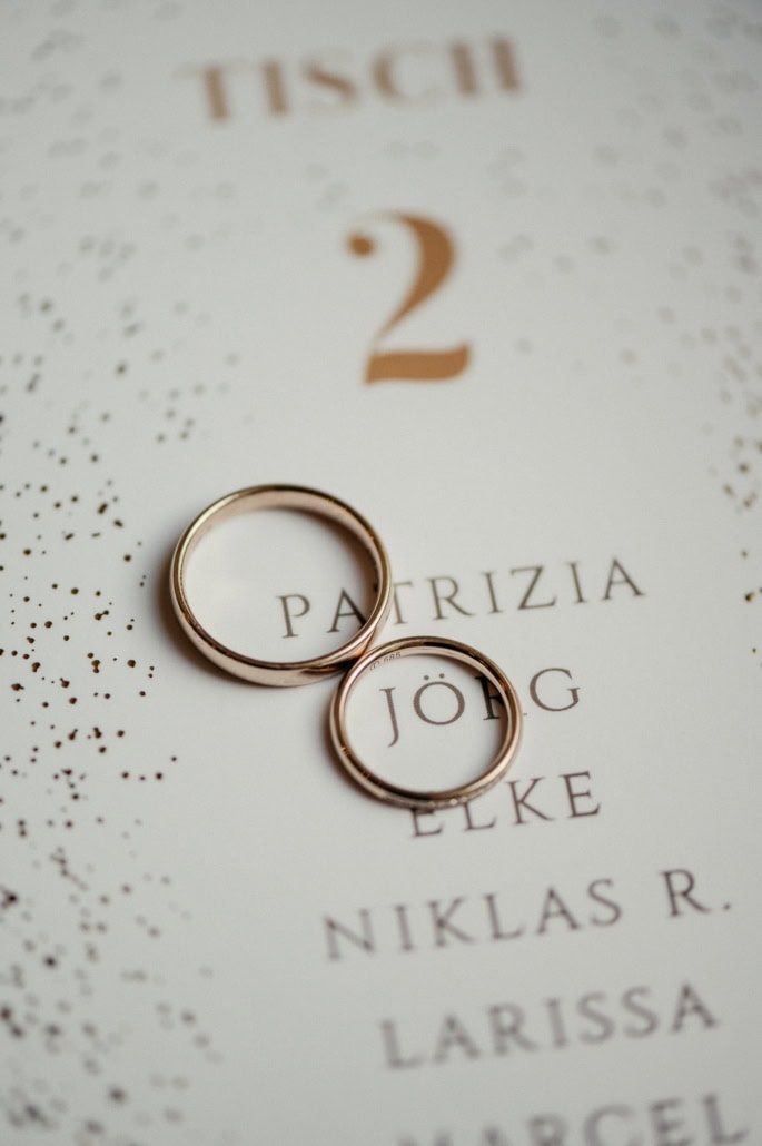 Hochzeitsringe liegen auf einer Sitzordnungskarte mit Namen der Gäste, symbolisieren Liebe und Zusam.