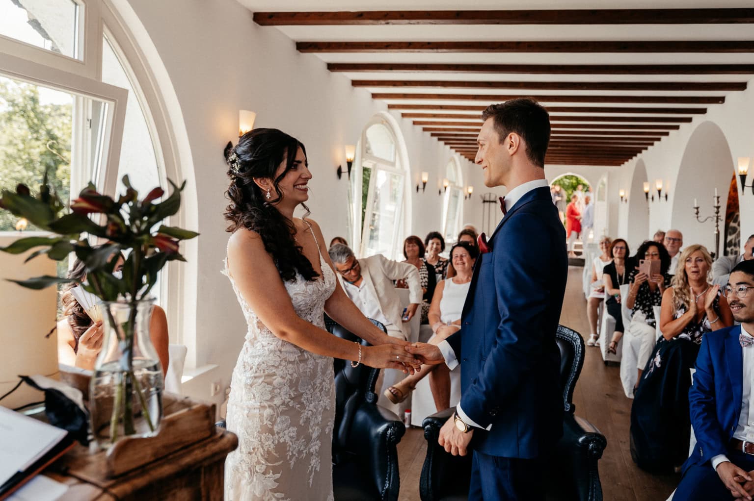 Braut und Bräutigam bei ihrer Hochzeit, Händchen haltend im festlichen Raum.
