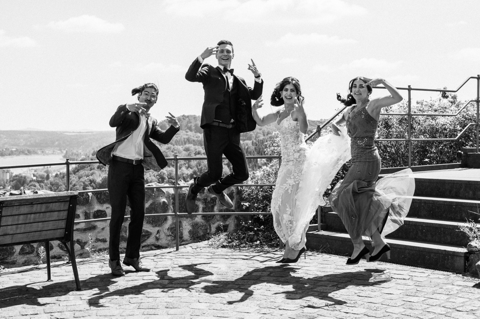 Hochzeitspaar beim fröhlichen Sprung auf einer Terrasse mit Stadtblick, lachend und tanzend.