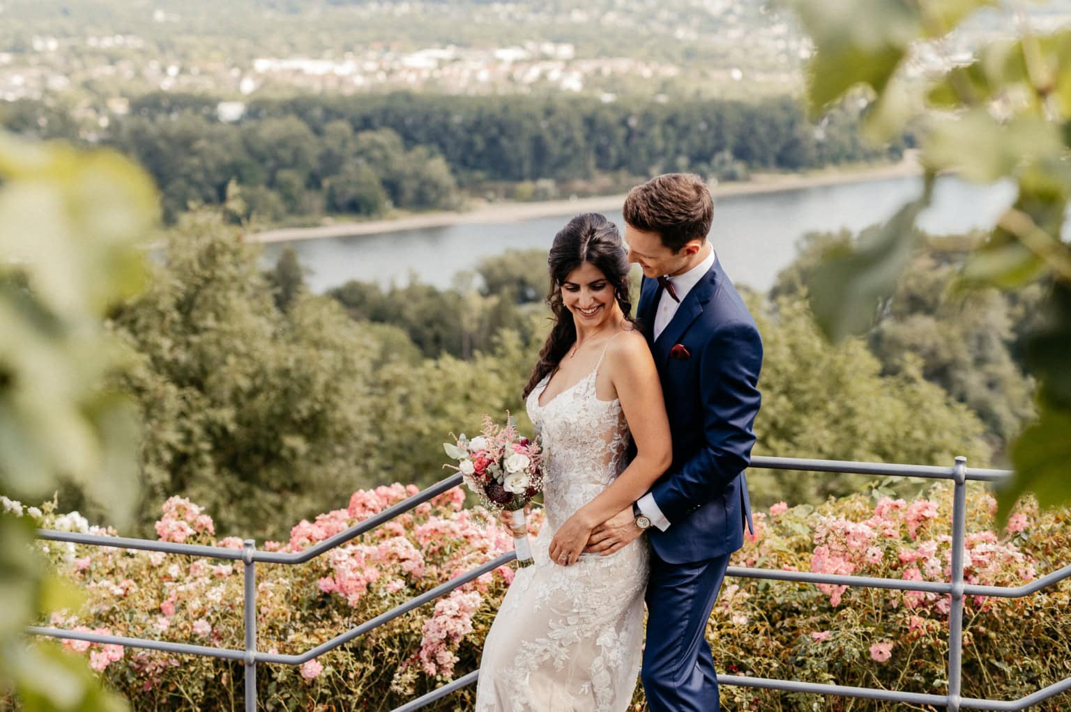 Braut und Bräutigam bei ihrer Hochzeit im Freien, umgeben von Blumen und Natur, mit Fluss im Hinterg.