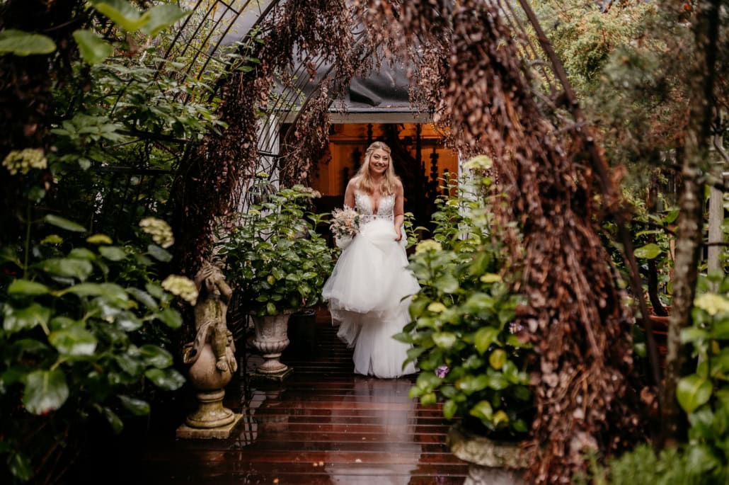 Braut im weißen Hochzeitskleid im Garten unter Laubbogen.