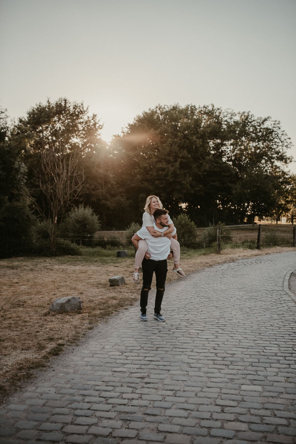 Frau trägt Kind auf den Schultern im Park bei Sonnenuntergang.