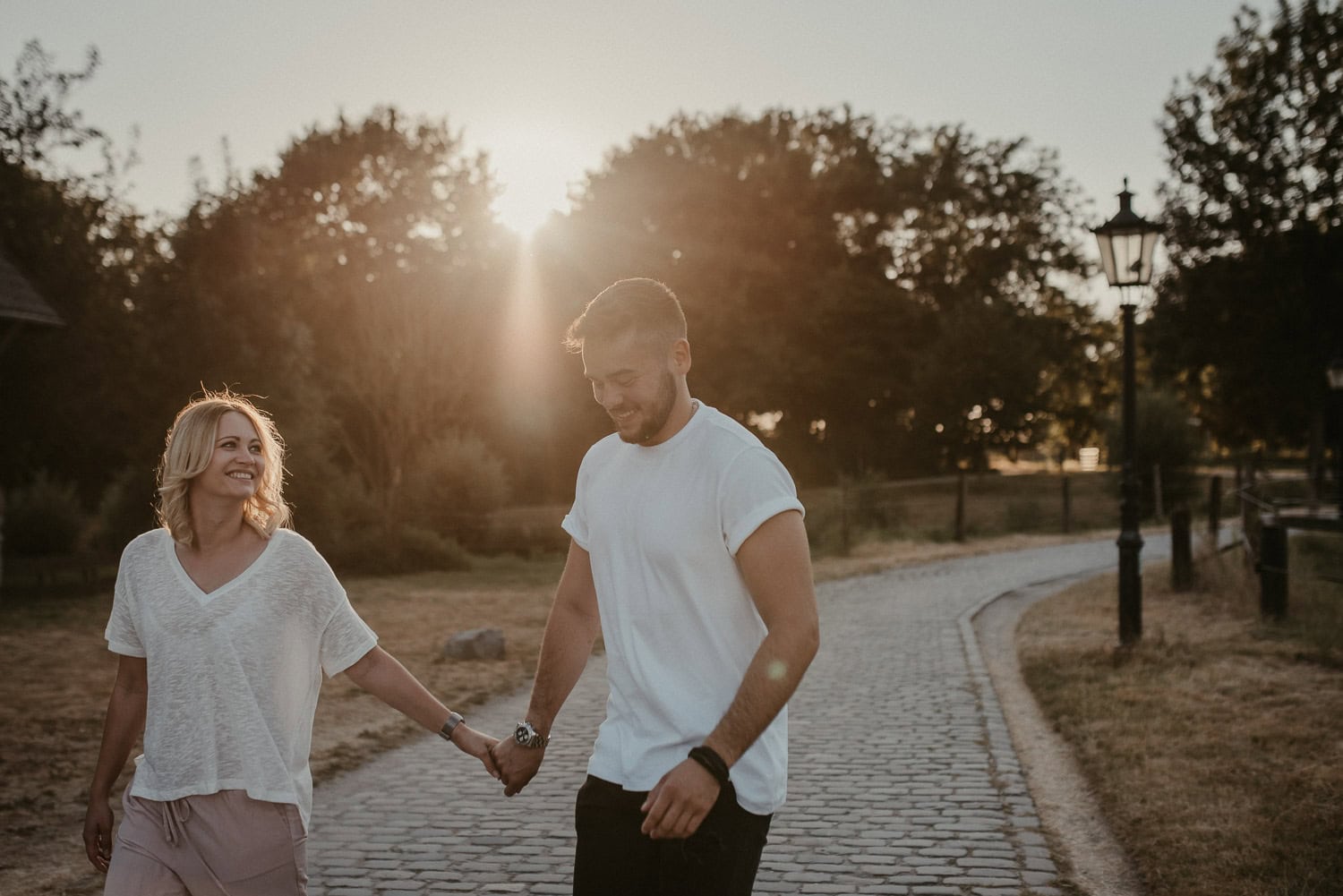 Zwei junge Menschen halten Händchen und lachen beim Spaziergang im Park.