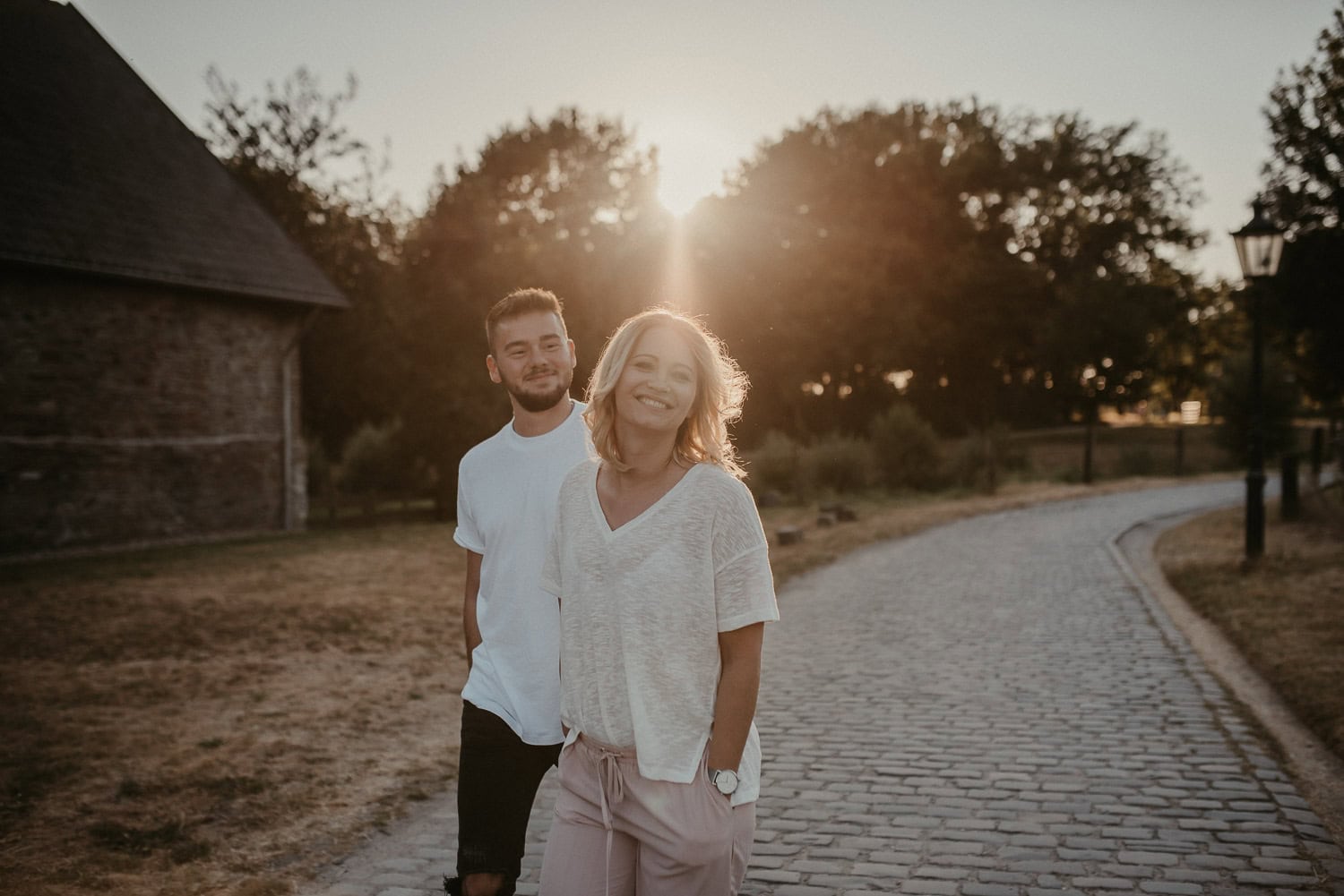 Lachendes Paar beim Spaziergang im Sonnenuntergang auf Kopfsteinpflaster.