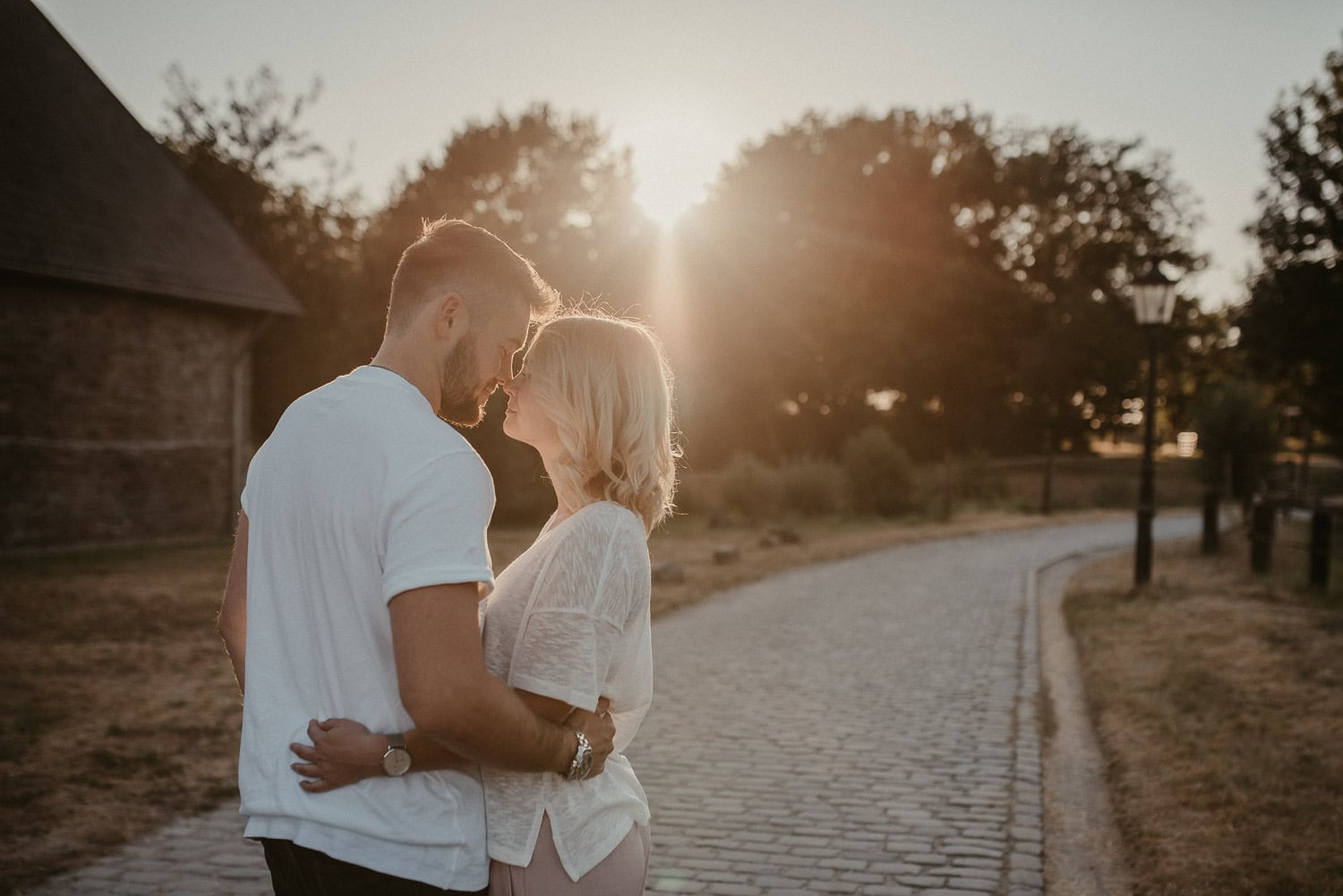 Hochzeitspaar umarmt sich auf einem Weg bei Sonnenuntergang im Freien.