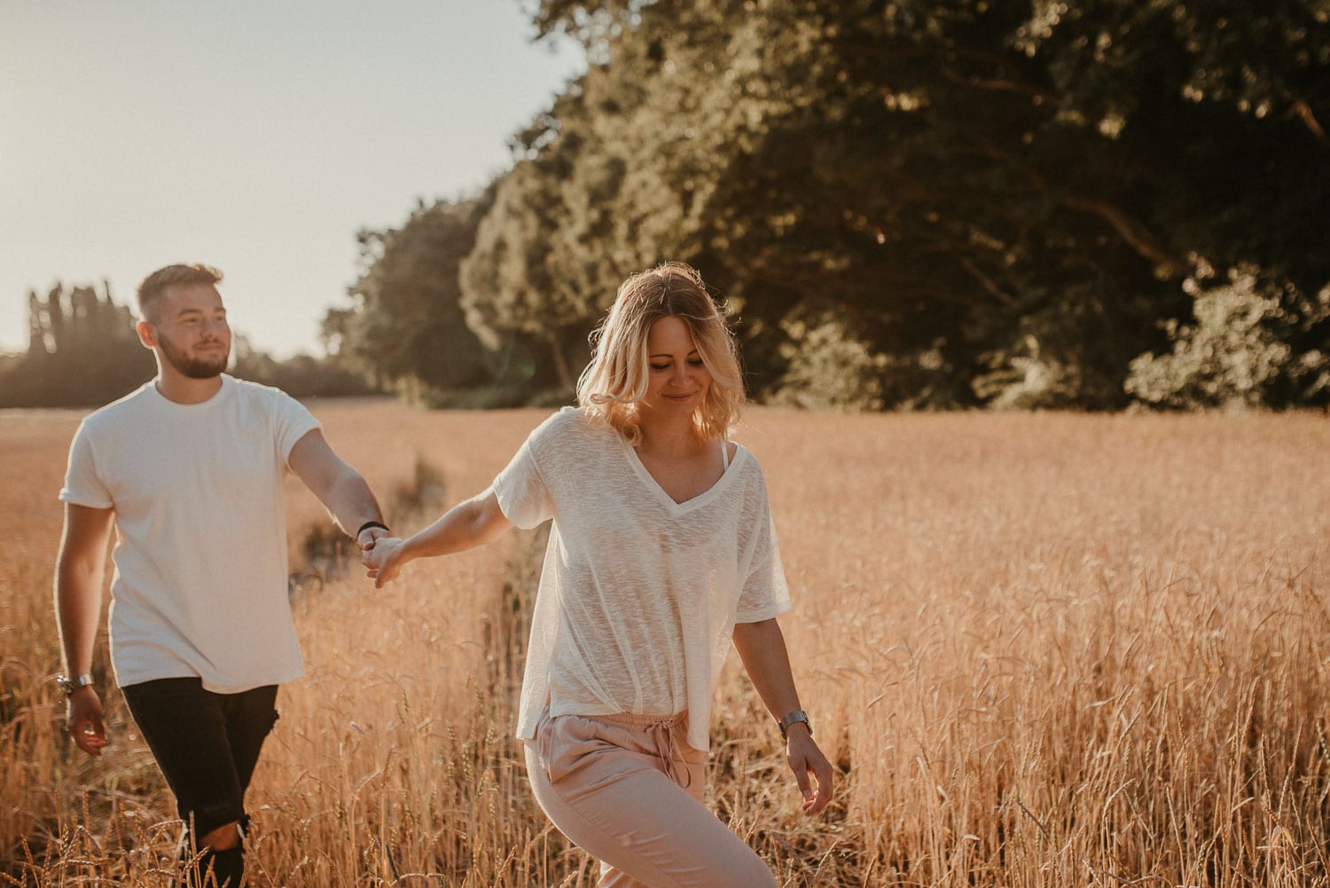 Paar beim Spaziergang im goldenen Feld bei Sonnenuntergang, Hand in Hand.